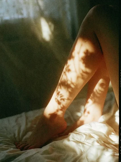 Late sunlight and leaf shadows falling across a woman resting on a bed