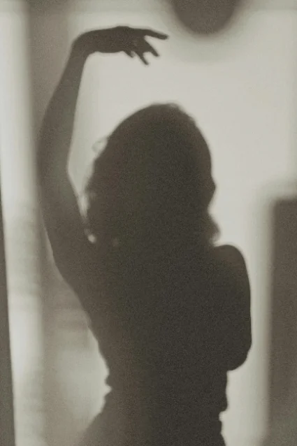 The shadow of a woman with one arm raised, on a sunlit wall